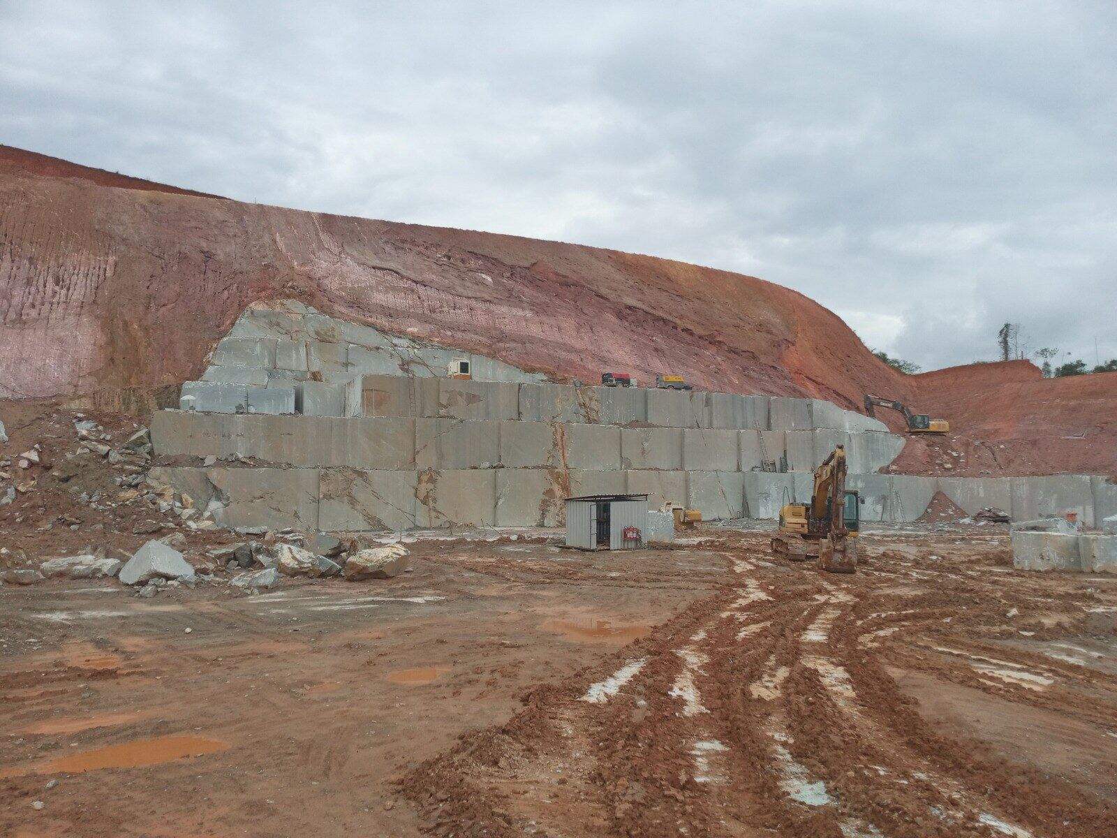 Quarry with soapstone blocks sawn out in steps beneath red earth, two excavators in front